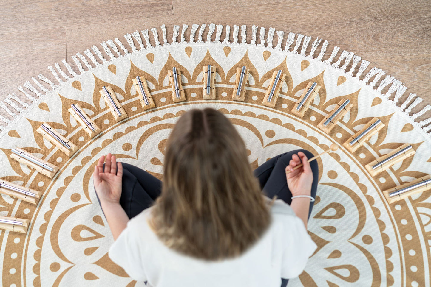 Person seated on a round meditation rug with sixteen planetary energy chimes arranged in a circle and a beater in hand. — for Carpe Diem Dream