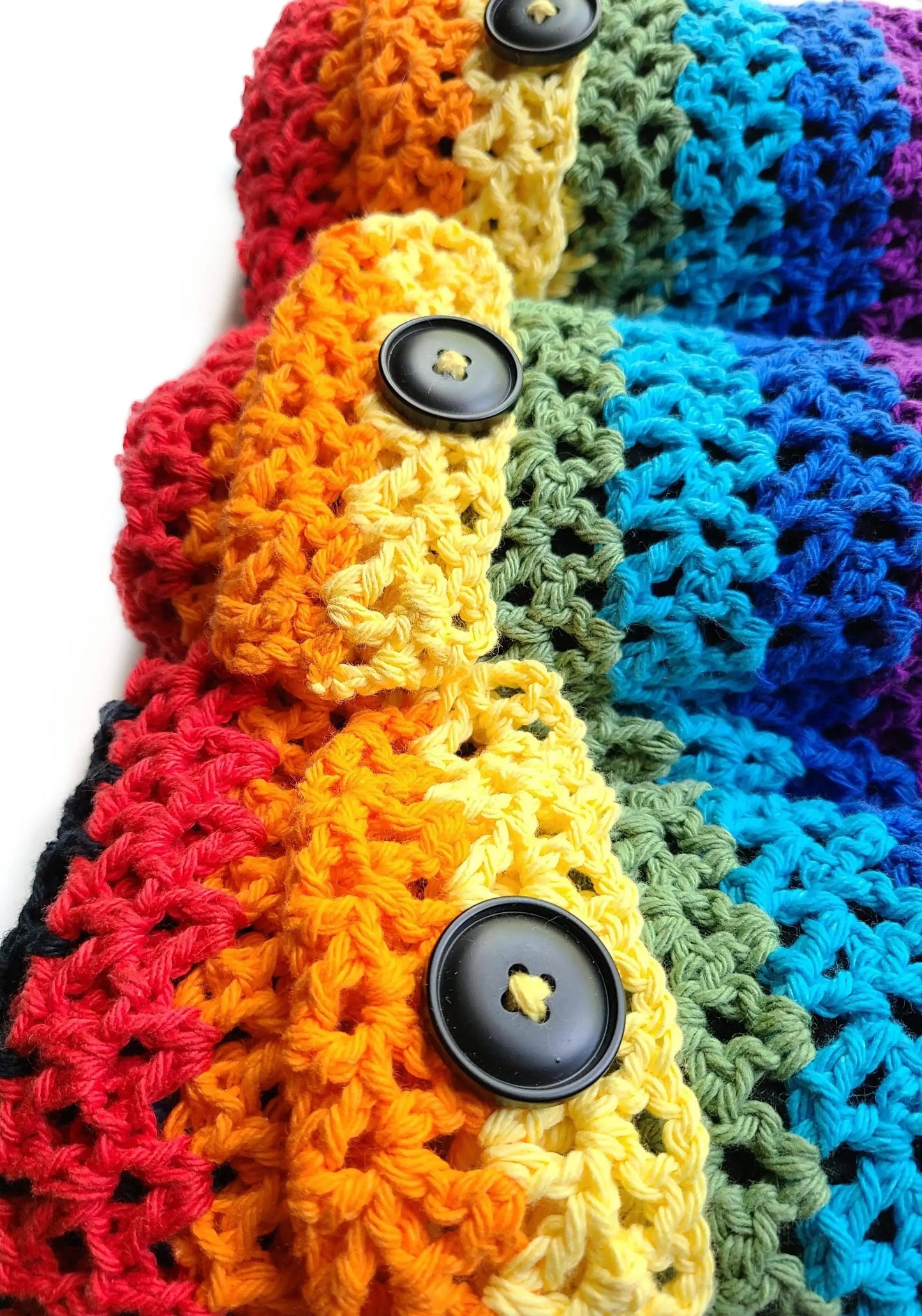 A close-up of a handmade chakra yoga mat bag shows the rainbow crochet pocket with black button closures against a white background. — for Carpe Diem Dream