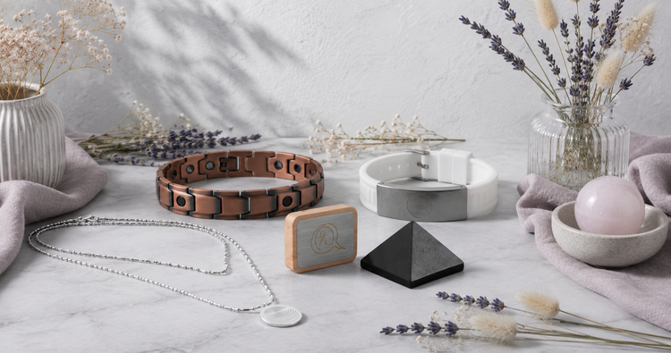 Therapeutic Wellness Devices collection featuring a defense pendant, EMF bracelet, copper magnetic bracelet, shungite pyramid, and Qi Me device in a bright botanical studio. — for Carpe Diem Dream