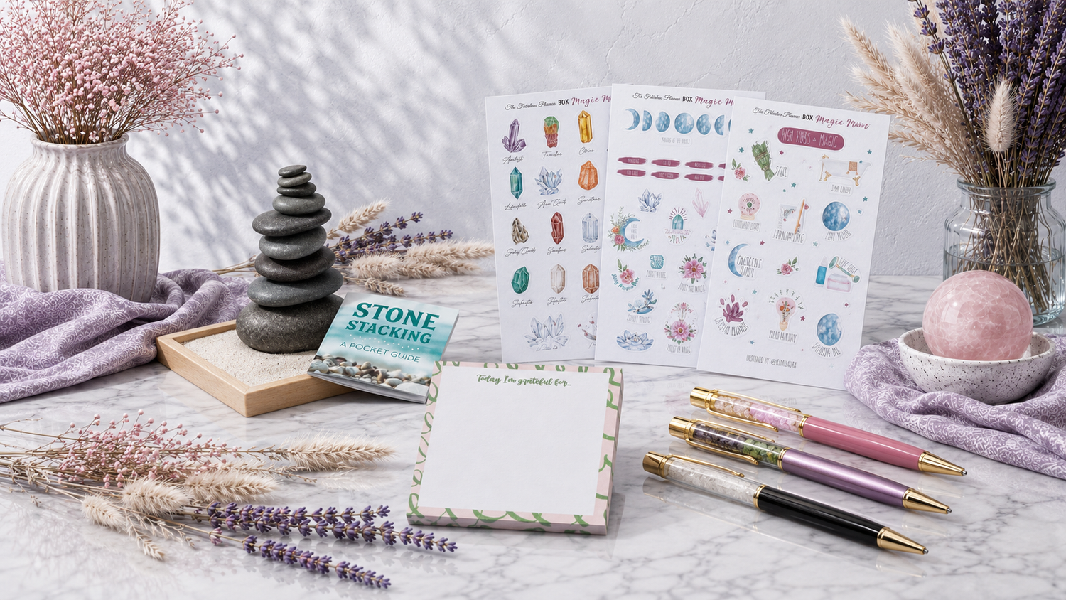 Communicate and Create collection image featuring gemstone pens, a gratitude notepad, moon and crystal sticker sheets, and a stone stacking set styled in a calm botanical setting. — for Carpe Diem Dream