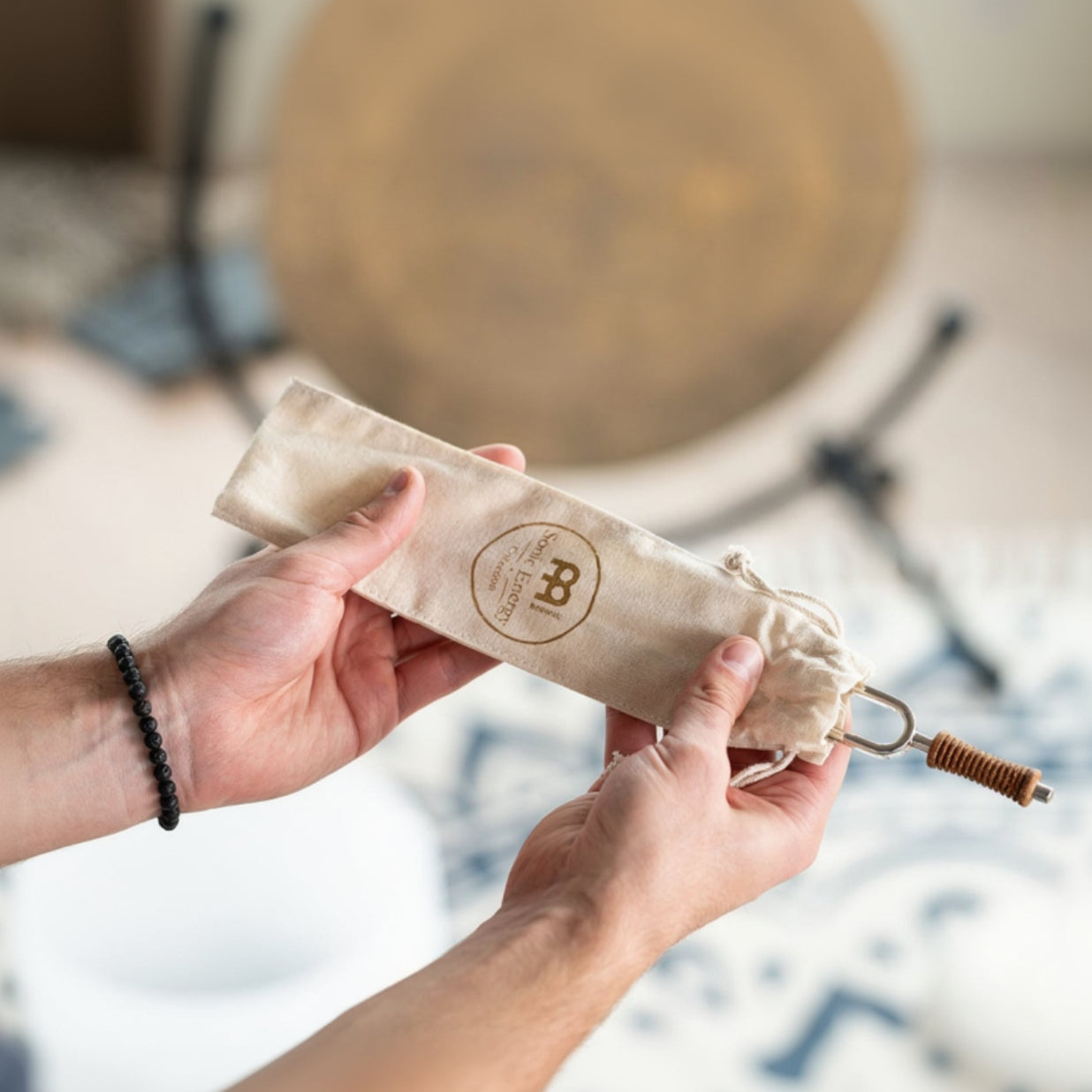 Hands holding a cotton storage pouch with a tuning fork partially visible and a gong blurred in the background. — for Carpe Diem Dream