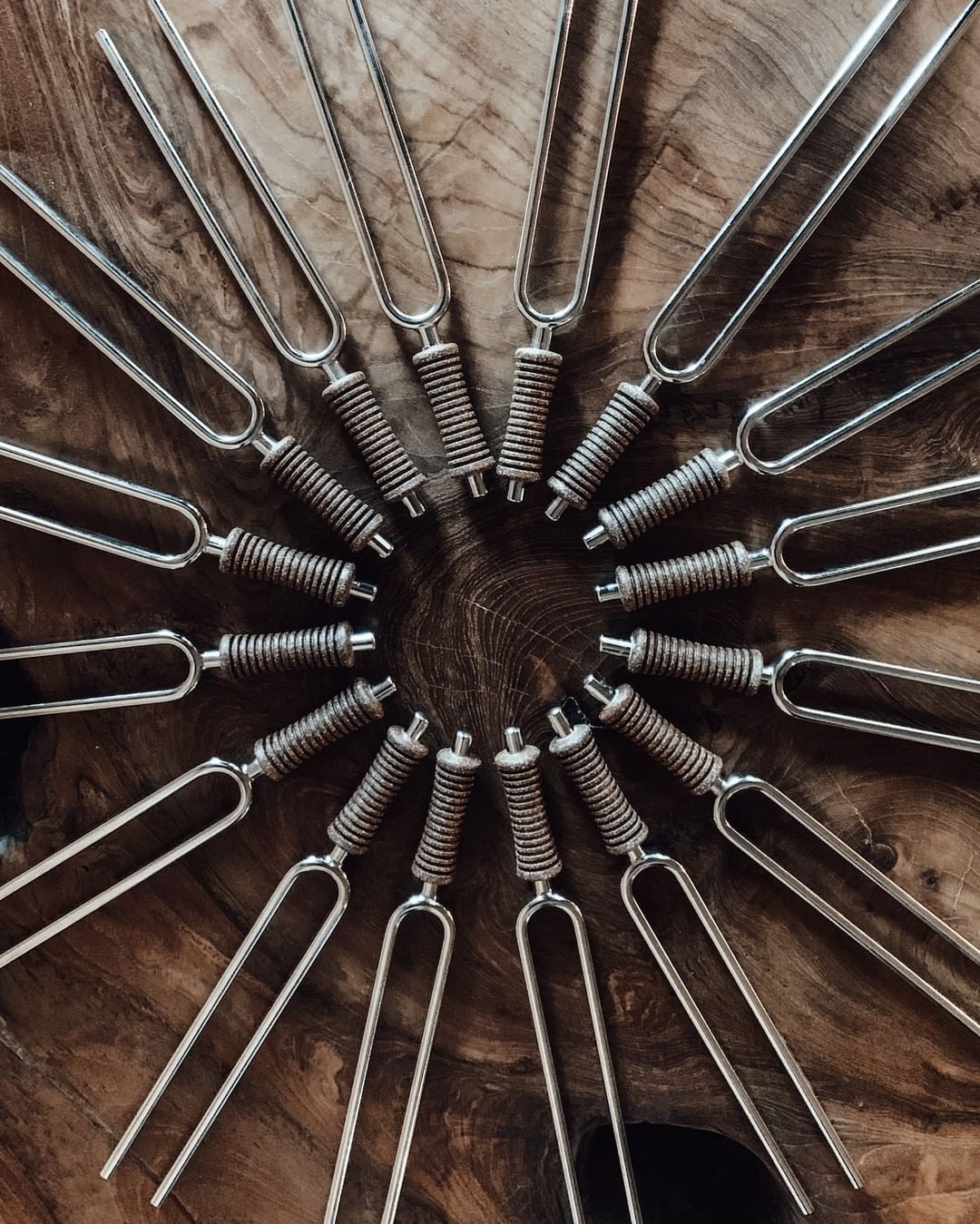 Sixteen metal planetary tuning forks arranged in a circular pattern on a wooden surface. — for Carpe Diem Dream