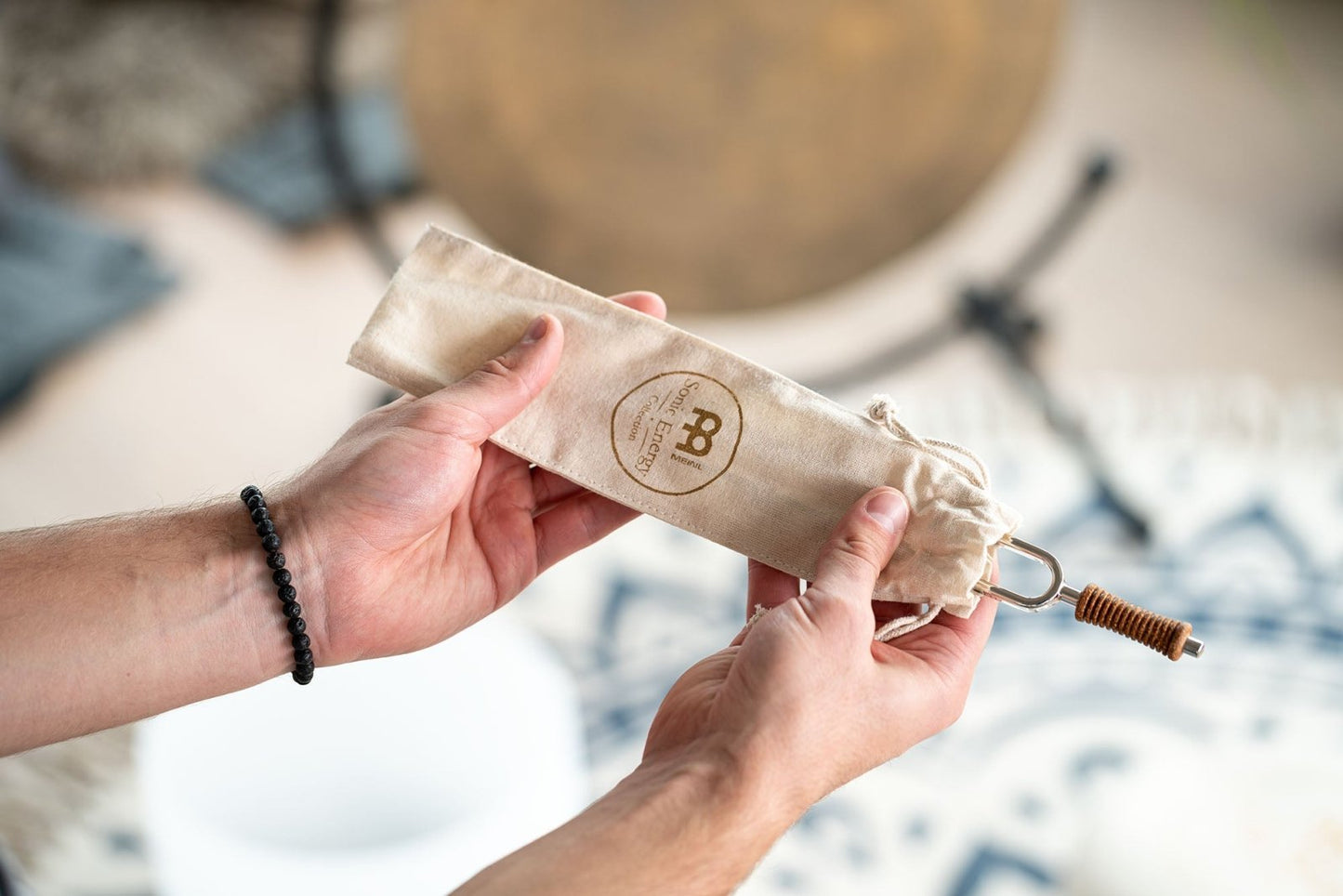 Hands holding a beige fabric pouch with logo while removing a metal tuning fork with cork handle. — for Carpe Diem Dream