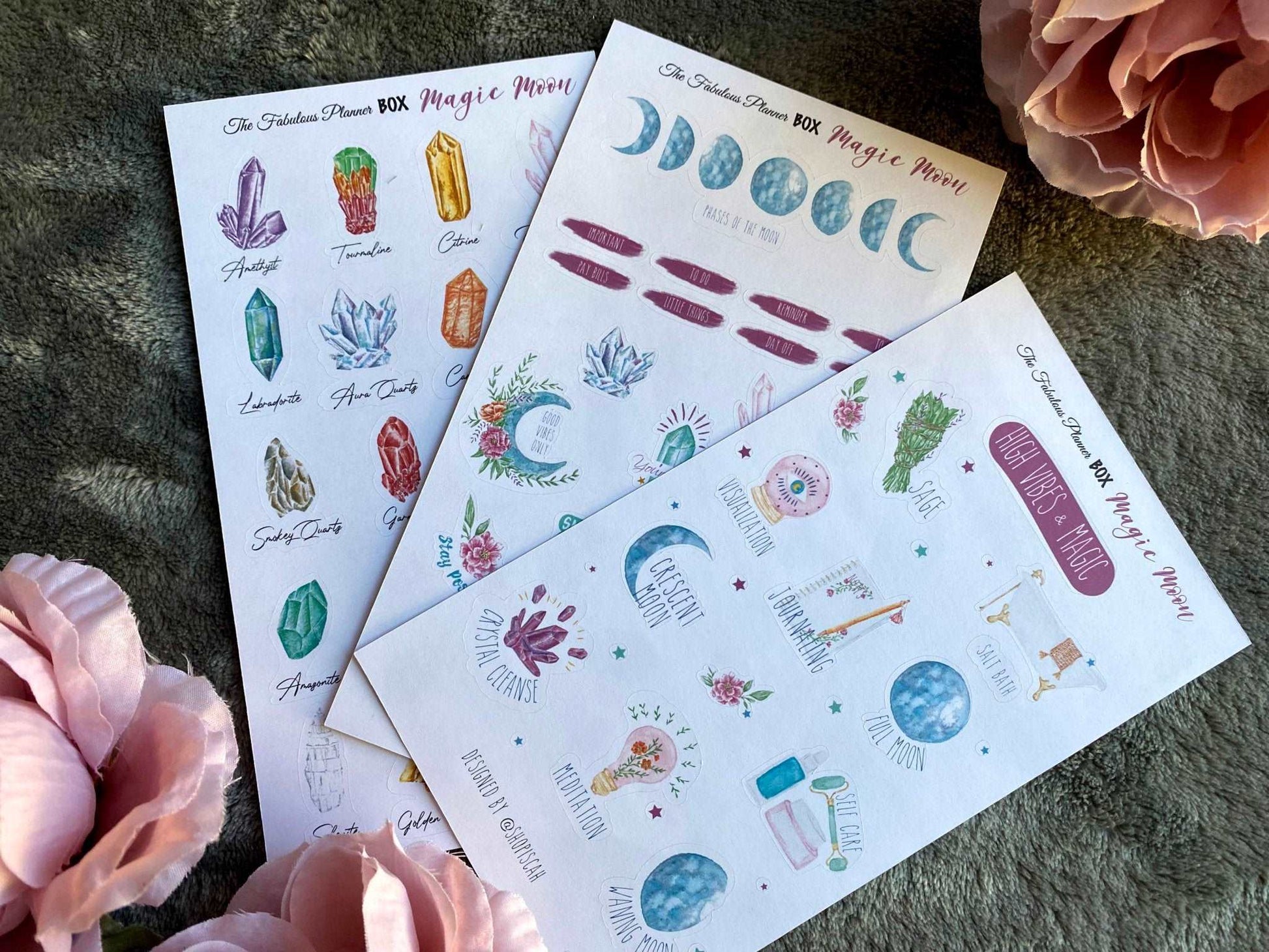Three 4x6 inch Magic Moon planner sticker sheets featuring moon phases, crystals, and celestial illustrations arranged on a textured surface with pink flowers — for Carpe Diem Dream