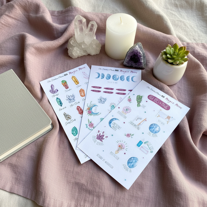 Three 4x6 inch Magic Moon planner sticker sheets arranged on soft pink fabric beside crystals, a candle, a small plant, and a notebook — for Carpe Diem Dream