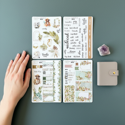Four 4x6 boho chic happy planner matte sticker sheets arranged on a green background with a hand for scale, a small planner, and an amethyst crystal. — for Carpe Diem Dream
