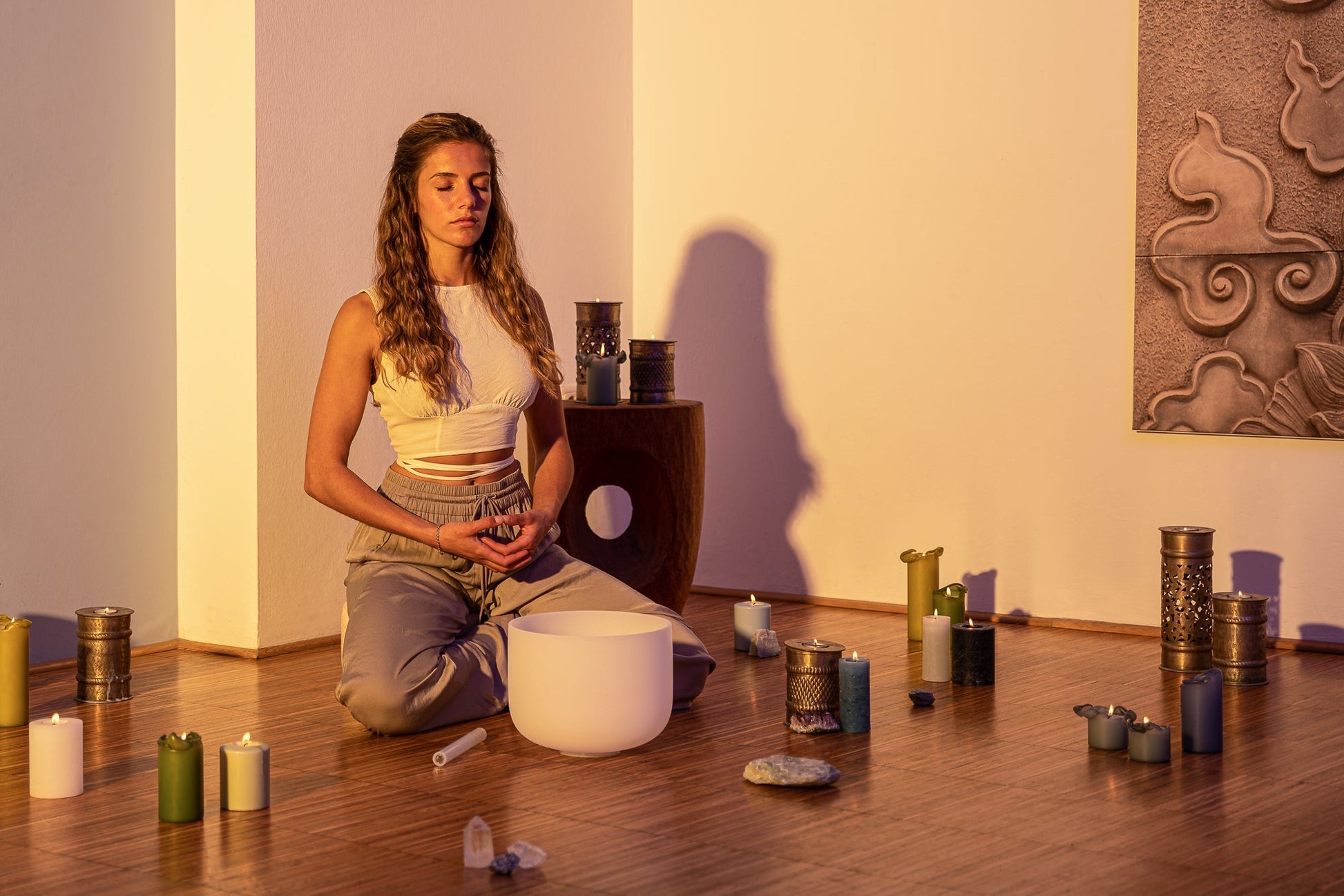 Woman seated in meditation pose beside a 10 inch white frosted crystal singing bowl on wooden floor with candles and warm lighting — for Carpe Diem Dream