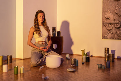 Woman seated in meditation pose beside a 10 inch white frosted crystal singing bowl on wooden floor with candles and warm lighting — for Carpe Diem Dream