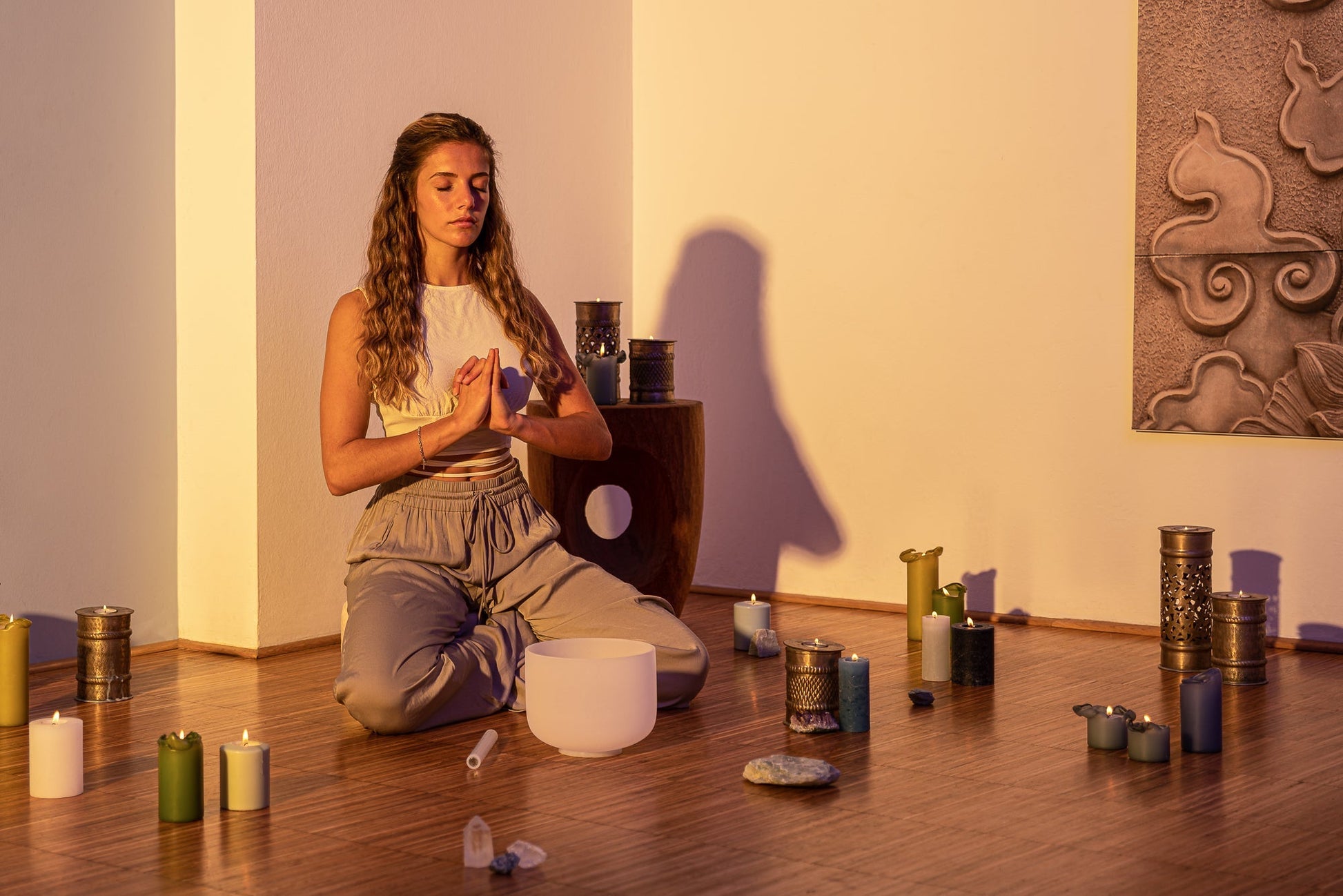 Woman seated in meditation pose beside an 8 inch white frosted crystal singing bowl on wooden floor with candles and warm lighting — for Carpe Diem Dream