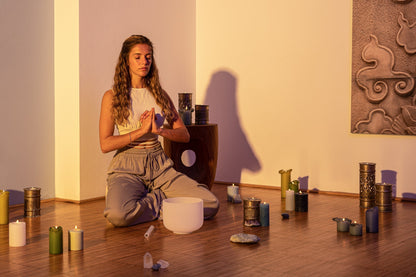 Woman seated in meditation pose beside an 8 inch white frosted crystal singing bowl on wooden floor with candles and warm lighting — for Carpe Diem Dream