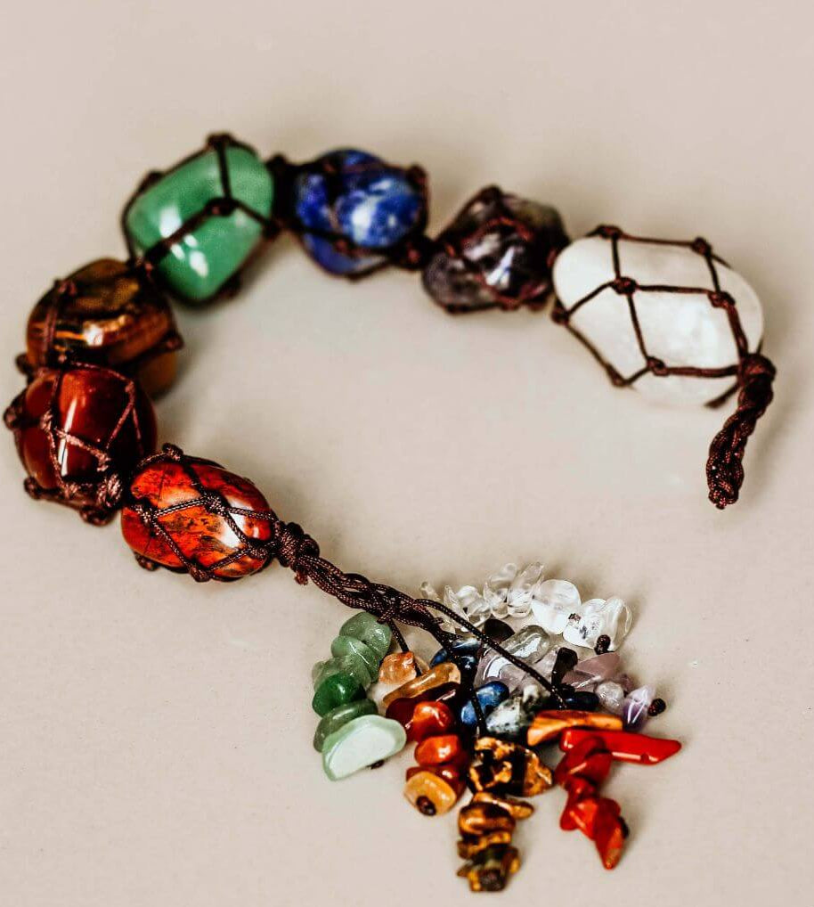 Colorful 7 chakra gemstone tassel hanging vertically against soft blush backdrop with crystal cluster detail. — for Carpe Diem Dream