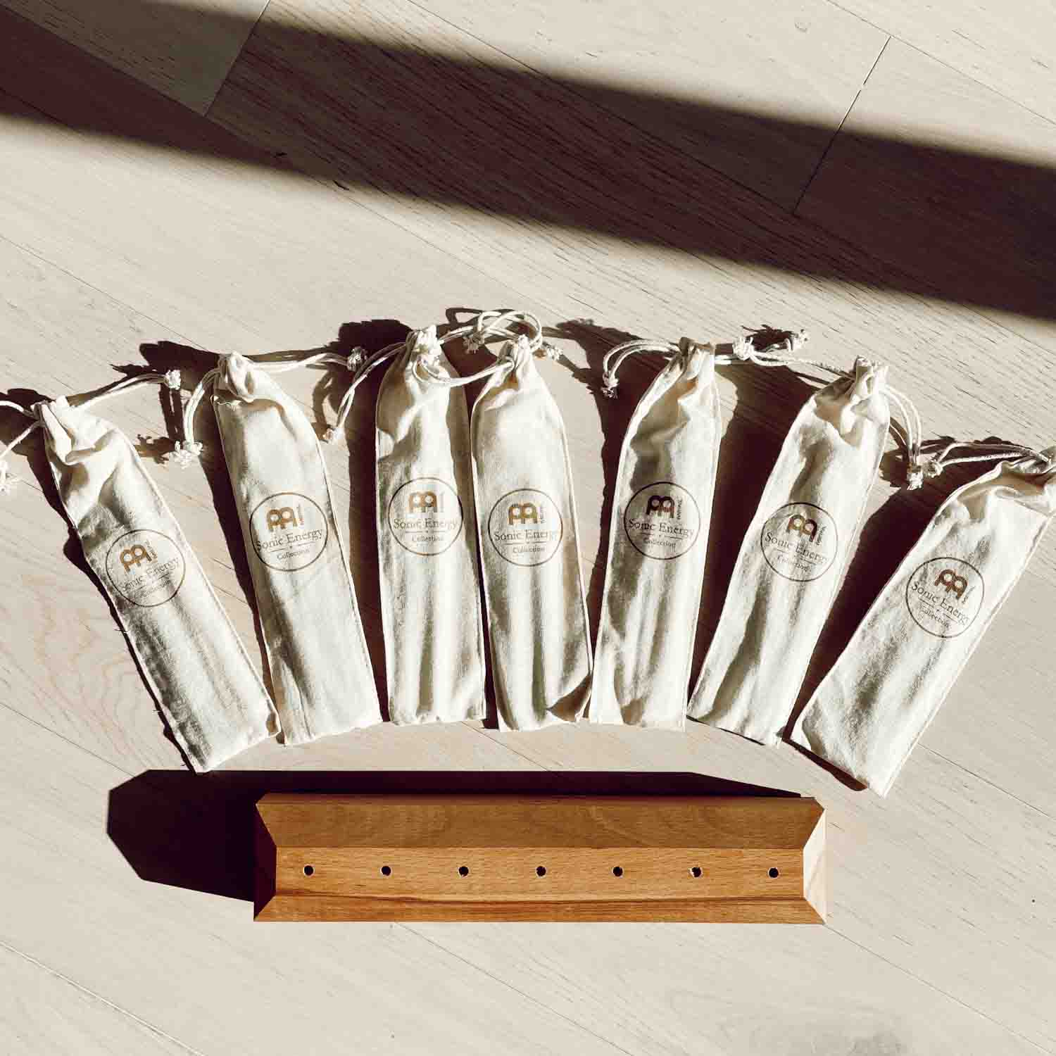 Seven cotton storage pouches and a wooden tuning fork base arranged in a top-down layout on a light surface. — for Carpe Diem Dream