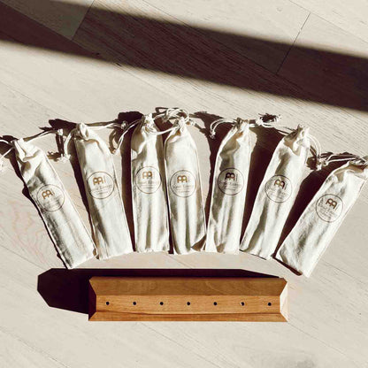 Seven cotton storage pouches and a wooden tuning fork base arranged in a top-down layout on a light surface. — for Carpe Diem Dream
