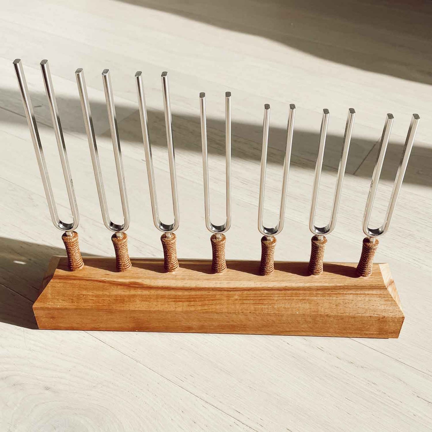 Seven chakra tuning forks with cork handles mounted on a wooden base on a light wood floor in natural sunlight. — for Carpe Diem Dream