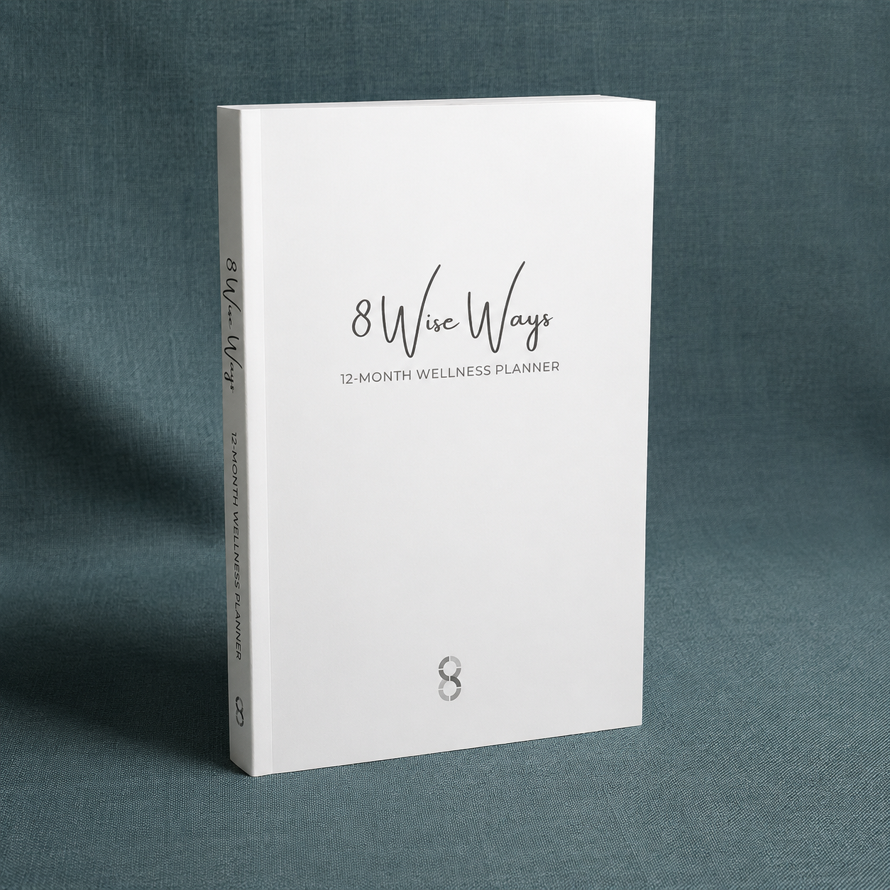 8 Wise Ways 12-Month Wellness Planner displayed upright on a teal-grey linen background with soft diffused lighting, designed to support wellbeing, reflection, healthy habits, and personal growth. — for Carpe Diem Dream