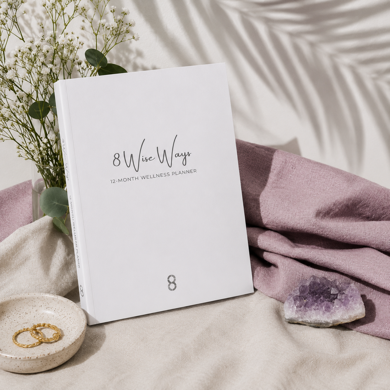 8 Wise Ways 12-Month Wellness Planner displayed on layered linen textiles with botanical accents and an amethyst crystal, creating a calm wellness-inspired setting for reflection, personal growth, and mindful living. — for Carpe Diem Dream