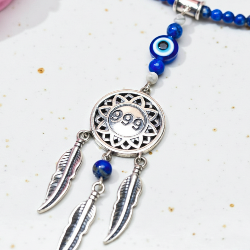 Silver dream catcher necklace with 999 angel number pendant and blue gemstone bead chain shown in a close-up view on white speckled background. — for Carpe Diem Dream
