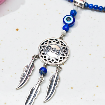 Silver dream catcher necklace with 999 angel number pendant and blue gemstone bead chain shown in a close-up view on white speckled background. — for Carpe Diem Dream

