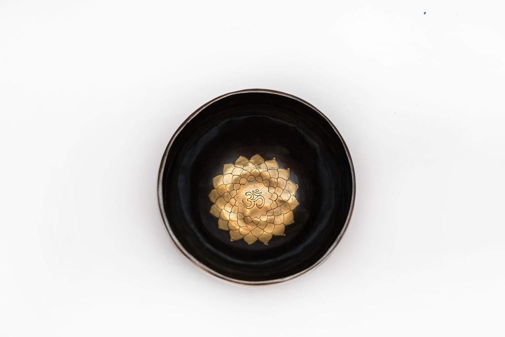 Top view of a black singing bowl with a gold Om symbol design on a white background. — for Carpe Diem Dream