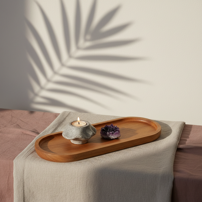 Acacia wood oval tray styled with a candle holder and amethyst crystal on layered neutral linens beneath soft botanical shadows. — for Carpe Diem Dream