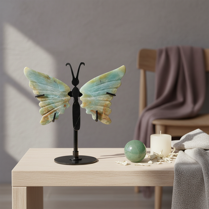 Amazonite crystal butterfly wings on a black stand displayed on a wooden table with a candle, green stone sphere, and soft textiles in a calm spa-inspired setting. — for Carpe Diem Dream