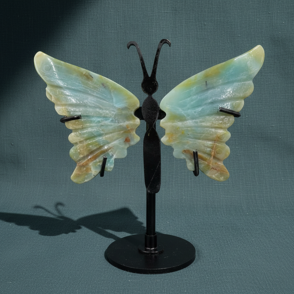 Amazonite crystal butterfly wings mounted on a black stand against a textured teal fabric background, highlighting the soft blue-green stone variation. — for Carpe Diem Dream