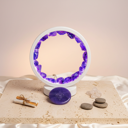 Amethyst halo lamp filled with natural crystals displayed upright on travertine pedestal with amethyst sphere and smooth stones against soft cream backdrop. — for Carpe Diem Dream