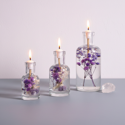 Three refillable Aquarius oil candles in different sizes displayed in a clean lineup on a neutral surface, each in a clear glass vessel with dried purple flowers inside and a lit flame. — for Carpe Diem Dream