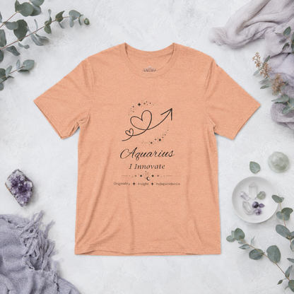 Aquarius Rising I Innovate zodiac T-shirt in Heather Peach with black celestial heart and arrow artwork and Originality, Insight, Independence text, styled in a cool-toned studio botanical flat lay. — for Carpe Diem Dream