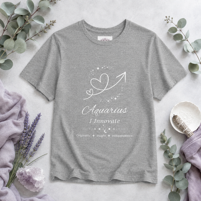 Aquarius Rising I Innovate zodiac T-shirt in Athletic Heather with white celestial heart and arrow artwork and Originality, Insight, Independence text, styled in a cool-toned studio botanical flat lay. — for Carpe Diem Dream