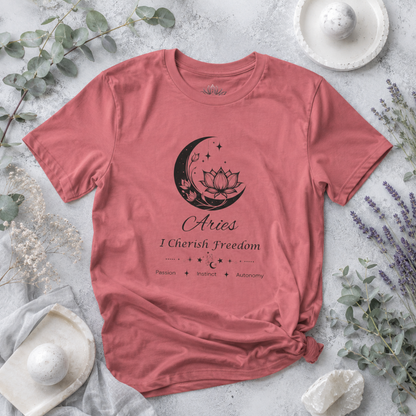 Aries Moon I Cherish Freedom zodiac T-shirt in mauve with black moon-inspired lotus, floral, and celestial artwork and Passion, Instinct, Autonomy text, styled in a cool-toned studio botanical flat lay. — for Carpe Diem Dream