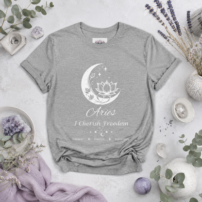 Aries Moon I Cherish Freedom zodiac T-shirt in Athletic Heather with white moon-inspired lotus, floral, and celestial artwork and Passion, Instinct, Autonomy text, styled in a cool-toned studio botanical flat lay with lavender, eucalyptus, crystals, and ceramic accents. — for Carpe Diem Dream
