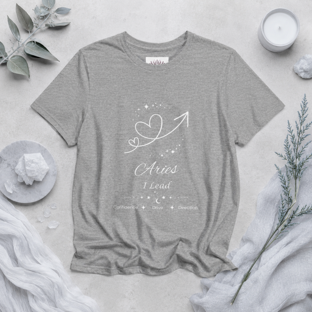 Aries Rising I Lead zodiac T-shirt in Athletic Heather with white celestial heart and arrow artwork and Confidence, Drive, Direction text, styled in a cool-toned studio botanical flat lay. — for Carpe Diem Dream