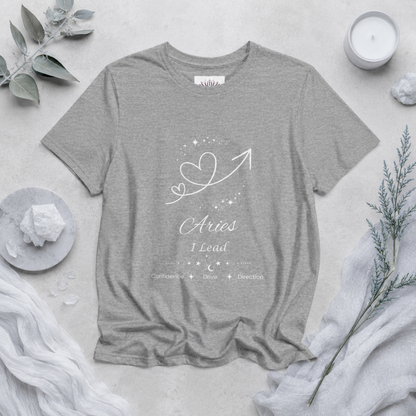 Aries Rising I Lead zodiac T-shirt in Athletic Heather with white celestial heart and arrow artwork and Confidence, Drive, Direction text, styled in a cool-toned studio botanical flat lay. — for Carpe Diem Dream