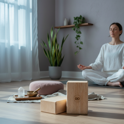 Two natural balsa wood yoga blocks displayed on a wood floor in front of a woman meditating in a calm room with plants, a mauve cushion, crystals, and a singing bowl. — for Carpe Diem Dream
