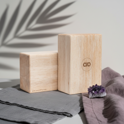Two natural balsa wood yoga blocks displayed on gray and mauve fabric beside an amethyst crystal with soft palm leaf shadows on a white wall. — for Carpe Diem Dream