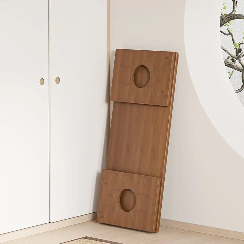 A bamboo folding table shown in its folded, compact form leaning against a wall in a bright, minimal interior. — for Carpe Diem Dream