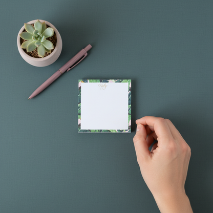 Square banana leaf border sticky note pad shown from above on a muted teal surface with a hand reaching toward it and a small succulent nearby. — for Carpe Diem Dream