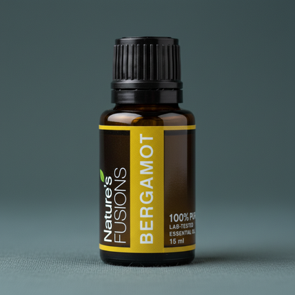 A close-up of a 15ml amber glass bottle of Bergamot essential oil with a black ribbed cap and yellow label displayed on a muted teal surface. — for Carpe Diem Dream