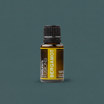 A 15ml amber glass bottle of Bergamot essential oil with a black ribbed cap and yellow label displayed upright on a muted teal background. — for Carpe Diem Dream
