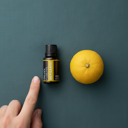 A hand pointing to a 15ml bottle of Bergamot essential oil beside a whole lemon on a muted teal background. — for Carpe Diem Dream
