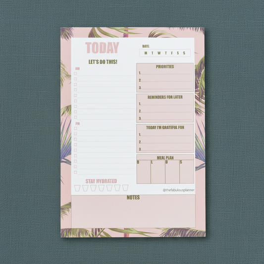 Large 7x10 pink tropical leaves daily planner notepad with structured sections for priorities, reminders, gratitude, meal planning, water tracking, and notes displayed upright on a muted teal textured background — for Carpe Diem Dream