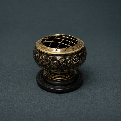 Black-and-antique-gold brass resin incense burner with a domed grid screen and black wooden coaster on a textured dark teal linen backdrop. — for Carpe Diem Dream