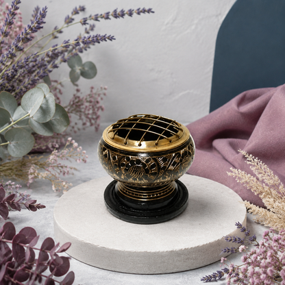 Black-and-antique-gold brass resin incense burner displayed on pale stone with lavender, eucalyptus, blush botanicals, mauve textile, and a dark teal studio accent. — for Carpe Diem Dream