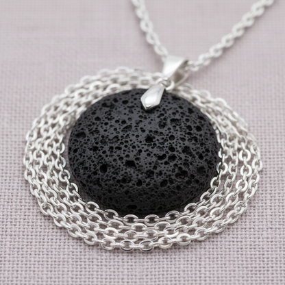 A close-up view of a round black lava stone essential oil necklace showing the porous volcanic texture and silver chain detail. — for Carpe Diem Dream