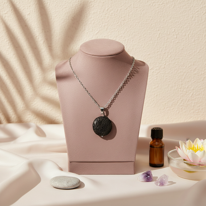 A round black lava stone essential oil necklace displayed on a blush jewelry stand with an amber oil bottle, crystal accents, and a lotus bowl on a soft neutral surface. — for Carpe Diem Dream