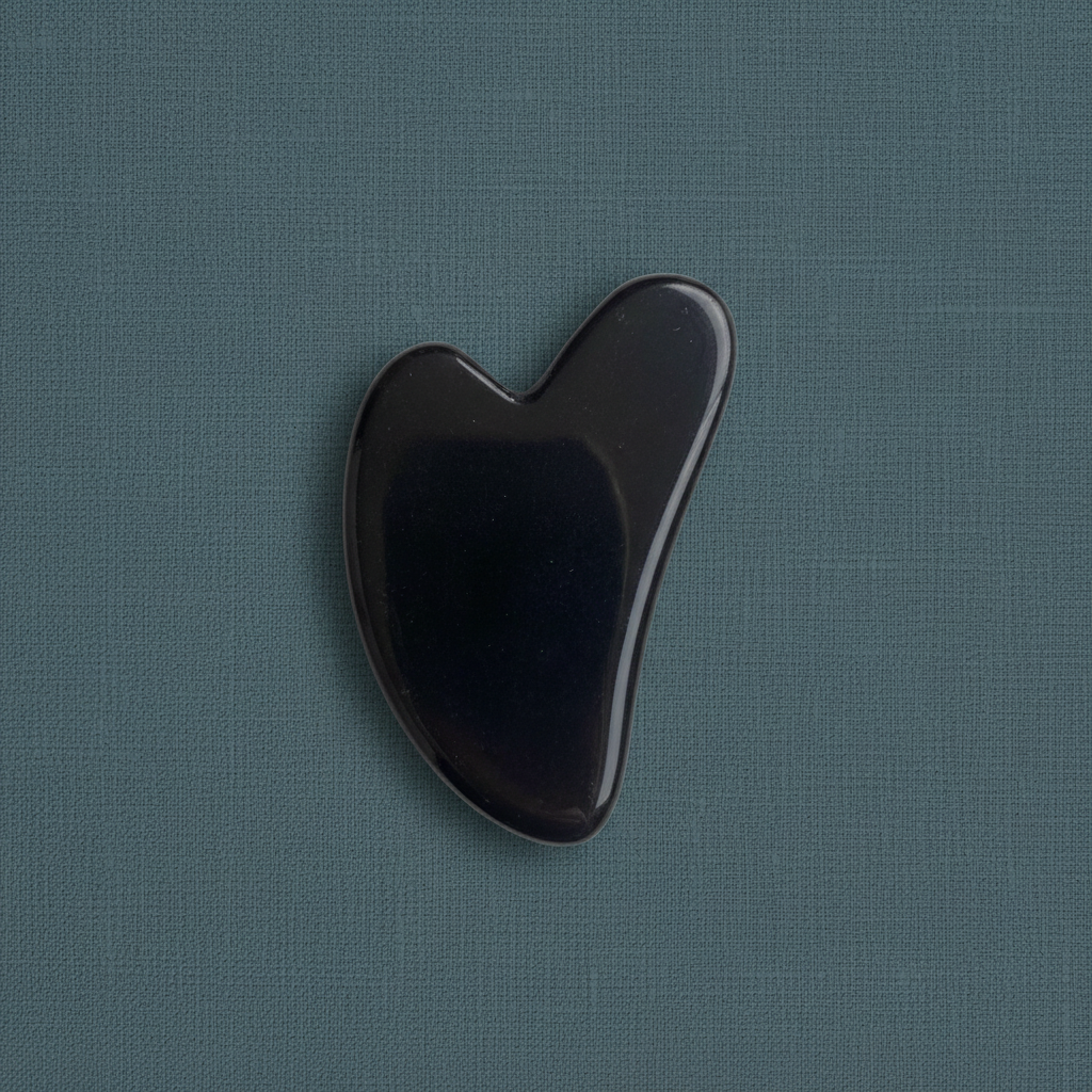 A black obsidian gua sha facial tool displayed on a muted teal linen background with soft lighting. — for Carpe Diem Dream