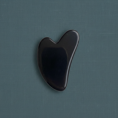 A black obsidian gua sha facial tool displayed on a muted teal linen background with soft lighting. — for Carpe Diem Dream