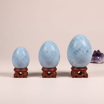 Three polished blue celestite crystal eggs in different sizes displayed on wooden stands against a soft neutral background. — for Carpe Diem Dream