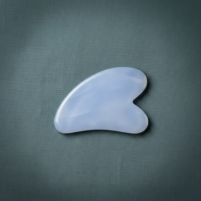 A blue chalcedony gua sha facial tool displayed on a muted teal linen background with soft natural lighting. — for Carpe Diem Dream